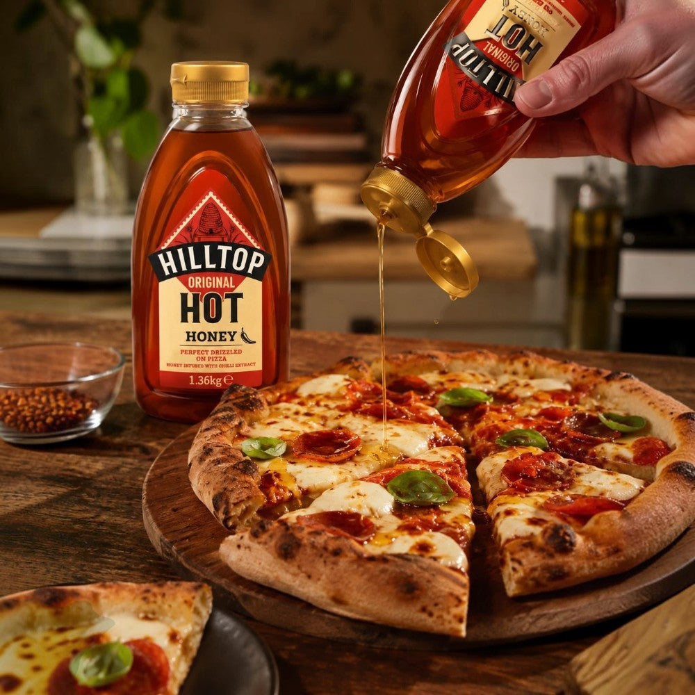 Hilltop Original Hot Honey with Chilli Extract 1.36kg bottle shown drizzling sweet and spicy honey over pizza